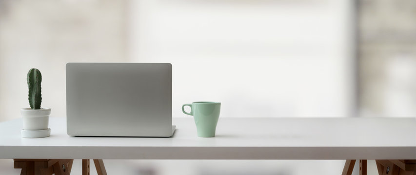 Cropped shot of simple workspace with laptop, cactus pot, mug and copy space on white table