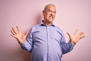 Middle age handsome hoary man wearing casual shirt standing over pink background crazy and mad shouting and yelling with aggressive expression and arms raised. Frustration concept.