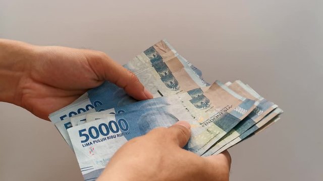 Counting indonesian rupiah money fifty thousand rupiahs (Rp. 50000) by hand in cash on white grey background