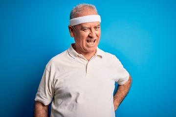 Middle age hoary sportsman doing sport wearing sportswear over isolated blue background winking...