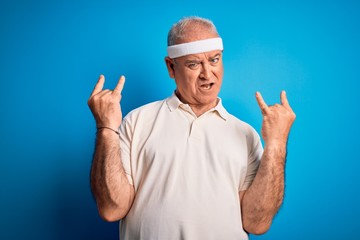 Middle age hoary sportsman doing sport wearing sportswear over isolated blue background shouting with crazy expression doing rock symbol with hands up. Music star. Heavy concept.