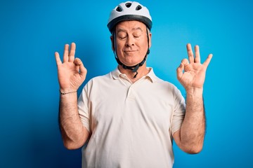 Middle age hoary cyclist man wearing bike security helmet over isolated blue background relax and smiling with eyes closed doing meditation gesture with fingers. Yoga concept.