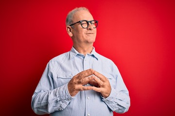Middle age handsome hoary man wearing casual striped shirt and glasses over red background Hands together and fingers crossed smiling relaxed and cheerful. Success and optimistic