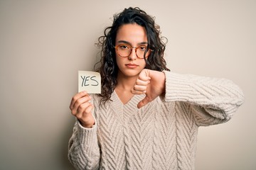 Young beautiful woman with curly hair holding reminder paper with yes word message with angry face,...