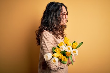 Young beautiful romantic woman with curly hair holding bouquet of yellow tulips looking to side, relax profile pose with natural face and confident smile.