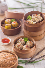 Soft and delicious shrimp shumai dimsum in stacked bamboo steamer for snack or tea break. Lit by natural light on white wood table and cloth.
