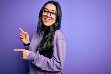 Young brunette woman wearing glasses over purple isolated background smiling and looking at the camera pointing with two hands and fingers to the side.