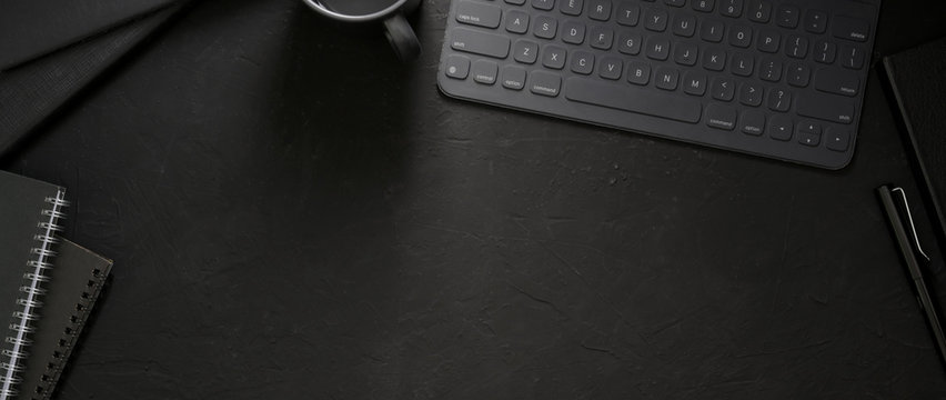 Top view of dark workspace with wireless device, office supplies and copy space
