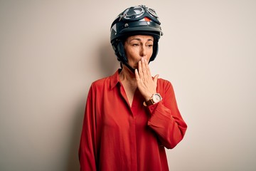 Middle age motorcyclist woman wearing motorcycle helmet over isolated white background bored yawning tired covering mouth with hand. Restless and sleepiness.