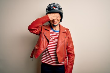 Fototapeta premium Middle age motorcyclist woman wearing motorcycle helmet and jacket over white background smiling and laughing with hand on face covering eyes for surprise. Blind concept.