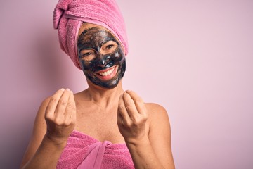 Middle age brunette woman wearing beauty black face mask over isolated pink background doing money gesture with hands, asking for salary payment, millionaire business
