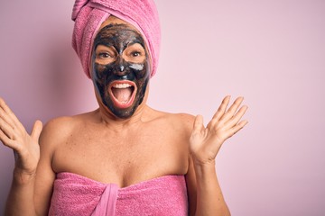 Middle age brunette woman wearing beauty black face mask over isolated pink background celebrating crazy and amazed for success with arms raised and open eyes screaming excited. Winner concept