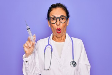 Middle age senior professional doctor woman holding syringe with medical vaccine scared in shock with a surprise face, afraid and excited with fear expression