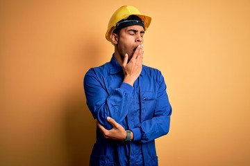 Young handsome african american worker man wearing blue uniform and security helmet bored yawning...