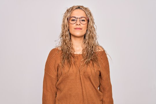 Young beautiful blonde woman wearing casual sweater and glasses over white background Relaxed with serious expression on face. Simple and natural looking at the camera.