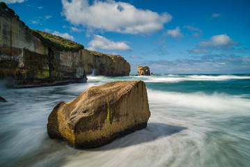Rock formations surrounded by ocean waves breaking against the rocky landscape of Tunnel Beach at...