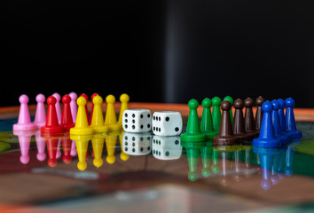 Closeup to a old white dices with color pawns over a board game with residential apartments at background