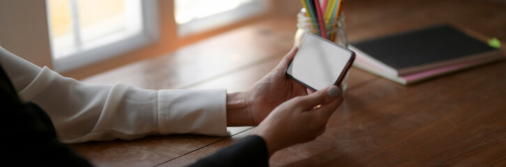 Cropped shot of female freelancer holding horizontal blank screen smartphone on wooden table