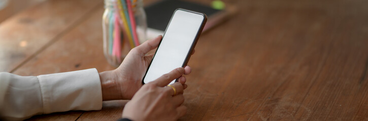 Cropped shot of female freelancer using blank screen smartphone on wooden desk