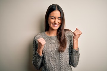 Young beautiful brunette woman wearing casual sweater over isolated white background excited for success with arms raised and eyes closed celebrating victory smiling. Winner concept.