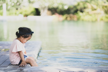 Little girl sitting at the swimming pool outdoor.