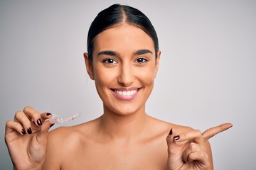 Young beautiful brunette woman holding dental aligner orthodontic to teeth corretion very happy pointing with hand and finger to the side