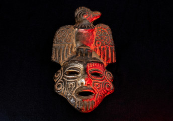An ancient ceramic pre columbus mask based in American indigenous tribes art iluminated by red light over black background 