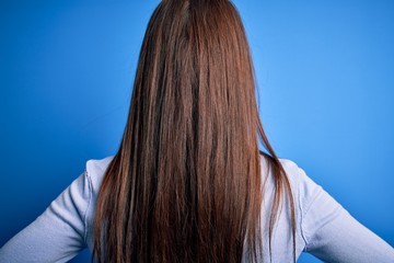 Young beautiful brunette woman wearing casual sweater standing over blue background standing backwards looking away with arms on body