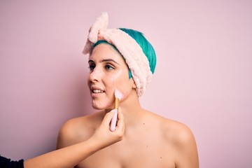 Close up of young beautiful woman doing cleansing procedure. Applying fresh cosmetic facial mask as wellness spa treatment.