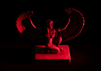 Closeup to a Isis. female old winged egyptian god mini figurine iluminated with red lights over...