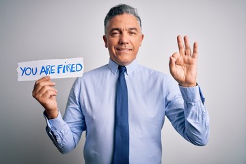 Middle age grey-haired man fired with problems holding paper with you are fired message doing ok sign with fingers, excellent symbol