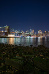 Naklejka premium Panoramic Cityscape View of New York City at night with illuminated skyscrapers and bridges inside urban city center