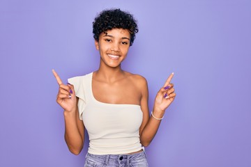 Young beautiful african american afro woman wearing casual t-shirt over purple background smiling confident pointing with fingers to different directions. Copy space for advertisement