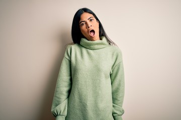 Young beautiful hispanic woman wearing green winter sweater over isolated background In shock face, looking skeptical and sarcastic, surprised with open mouth