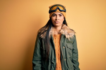 Young beautiful hispanic woman wearing ski glasses and coat for winter weather looking sleepy and tired, exhausted for fatigue and hangover, lazy eyes in the morning.