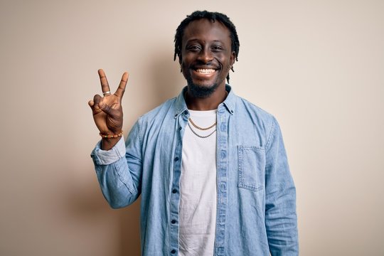 Young handsome african american man wearing casual denim shirt over white background smiling with happy face winking at the camera doing victory sign. Number two.