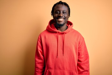 Young african american sporty man wearing sweatshirt with hoodie over yellow background with a...