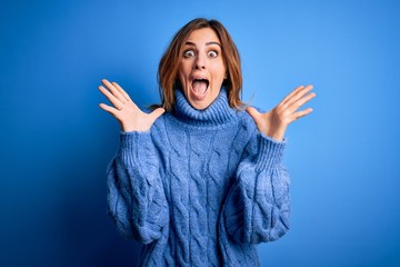 Young beautiful brunette woman wearing casual turtleneck sweater over blue background celebrating...
