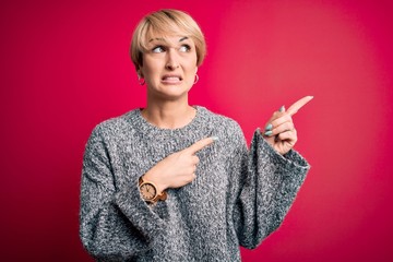 Young blonde woman with modern short hair wearing casual sweater over pink background Pointing...