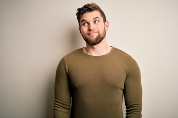 Young blond man with beard and blue eyes wearing green sweater over white background smiling looking to the side and staring away thinking.