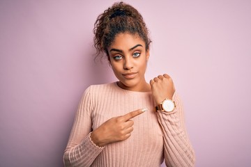 Young beautiful african american girl wearing casual sweater standing over pink background In hurry pointing to watch time, impatience, looking at the camera with relaxed expression