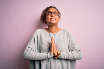 Young beautiful african american girl wearing sweater and glasses over pink background begging and...