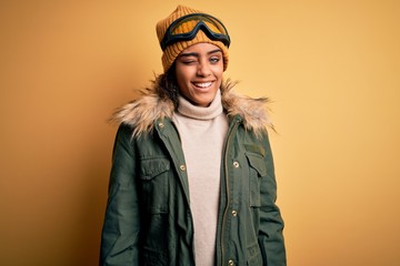 Young african american afro skier girl wearing snow sportswear and ski goggles winking looking at the camera with sexy expression, cheerful and happy face.