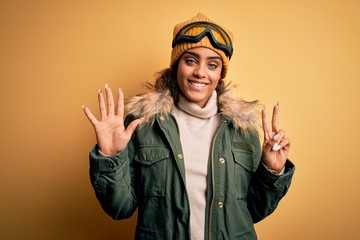 Young african american afro skier girl wearing snow sportswear and ski goggles showing and pointing up with fingers number seven while smiling confident and happy.