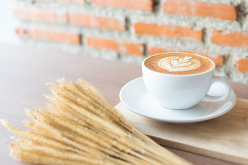 A cup of coffee in white cup with brown brick background, bunch of wheat at the front