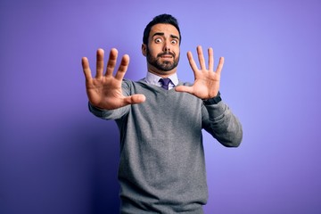Handsome businessman with beard wearing casual tie standing over purple background afraid and terrified with fear expression stop gesture with hands, shouting in shock. Panic concept.