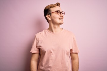 Obraz premium Young handsome redhead man wearing casual t-shirt standing over isolated pink background looking away to side with smile on face, natural expression. Laughing confident.