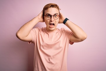 Young handsome redhead man wearing casual t-shirt standing over isolated pink background Crazy and scared with hands on head, afraid and surprised of shock with open mouth