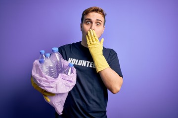 Young handsome redhead volunteer man doing volunteering holding bag with plastic bottles covering...