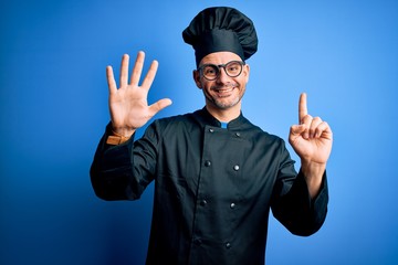 Young handsome chef man wearing cooker uniform and hat over isolated blue background showing and...